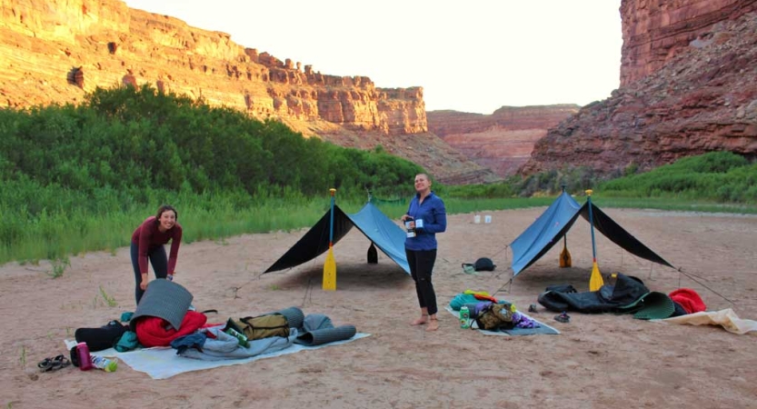 Two people stand at a campsite framed by red canyon walls. 